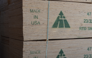 Large stack of industrial plywood stamped with brand and Made in USA in green paint.